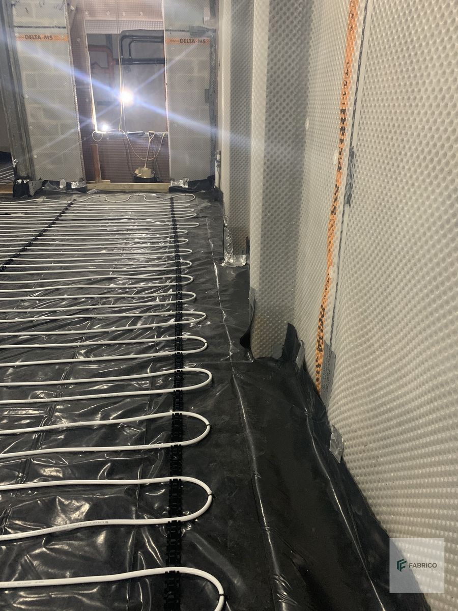 Underfloor heating loops alongside Delta MS cavity drain membrane with orange perimeter strip